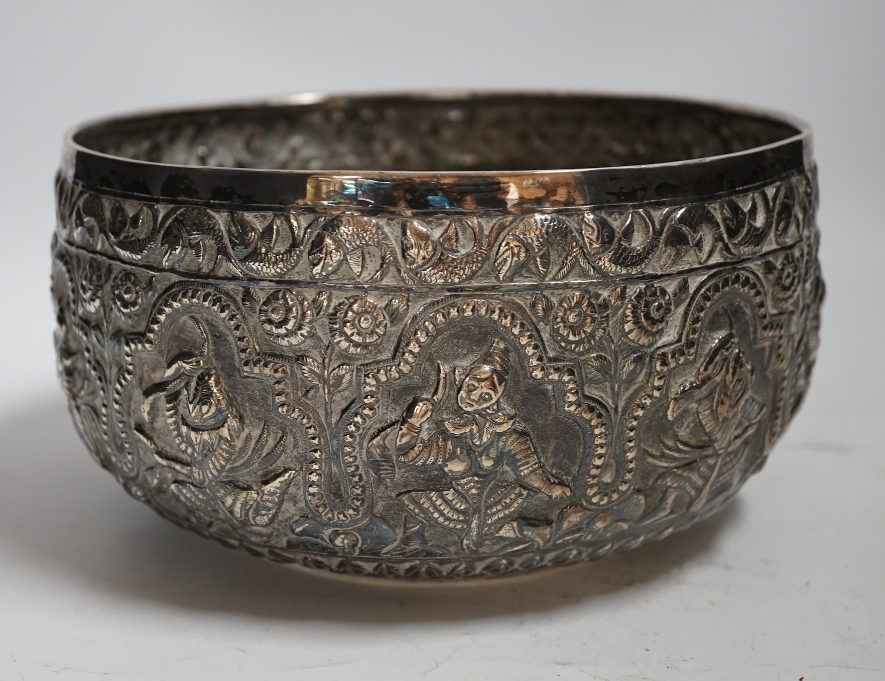 A 19th century Burmese embossed white metal bowl, decorated with figures and flowers, diameter 22.2cm, 22.9oz.